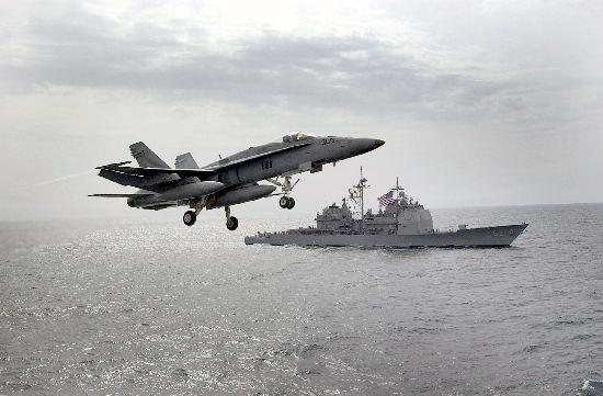 A $94 million F/A-18 Hornet flies past a U.S. warship